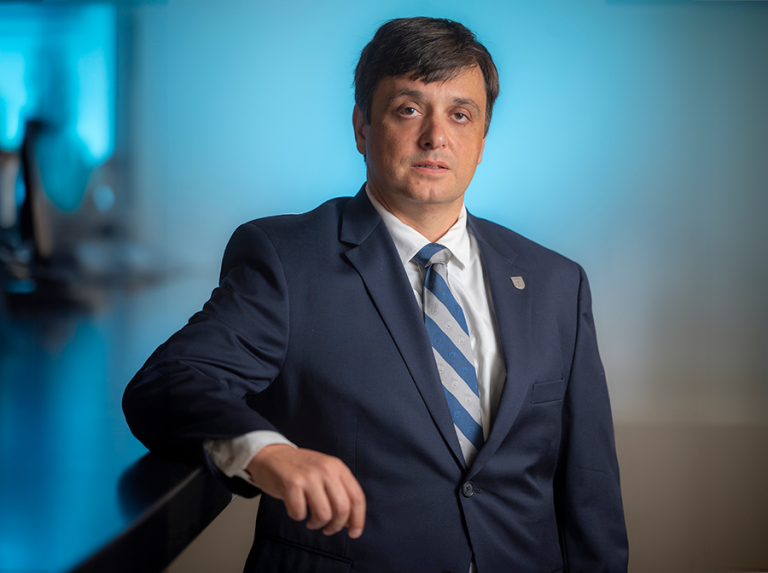 A man in a suit leans against a high counter top.