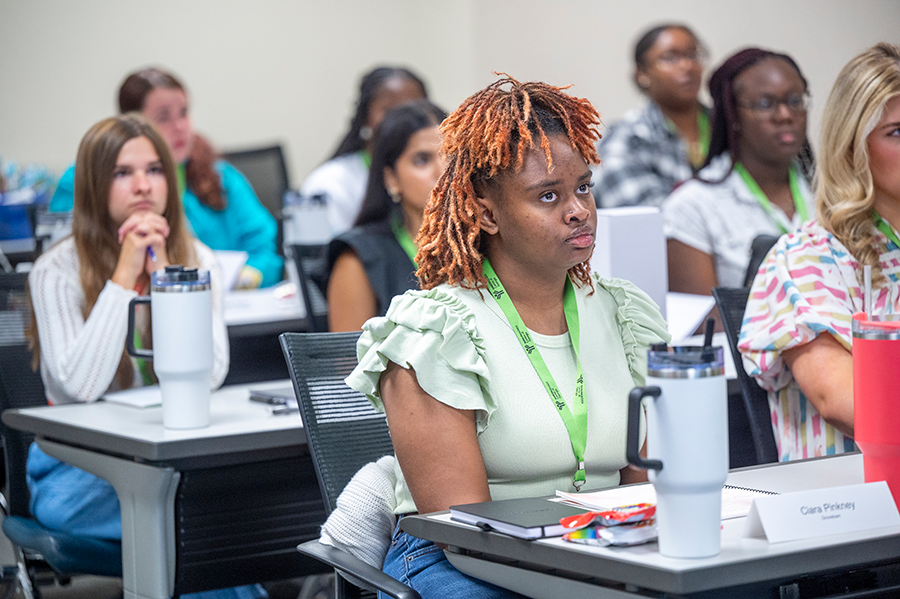 Female high school students sit in a college classroom and listen to a lecture.