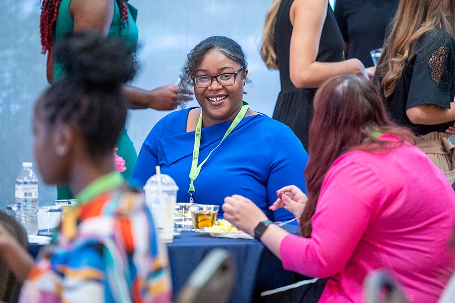 A young woman sits at a table with other women and talks during a meal.