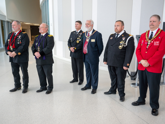 Six men in suits stand in a large atrium of a building. Each has numerous medals pinned to his chest.