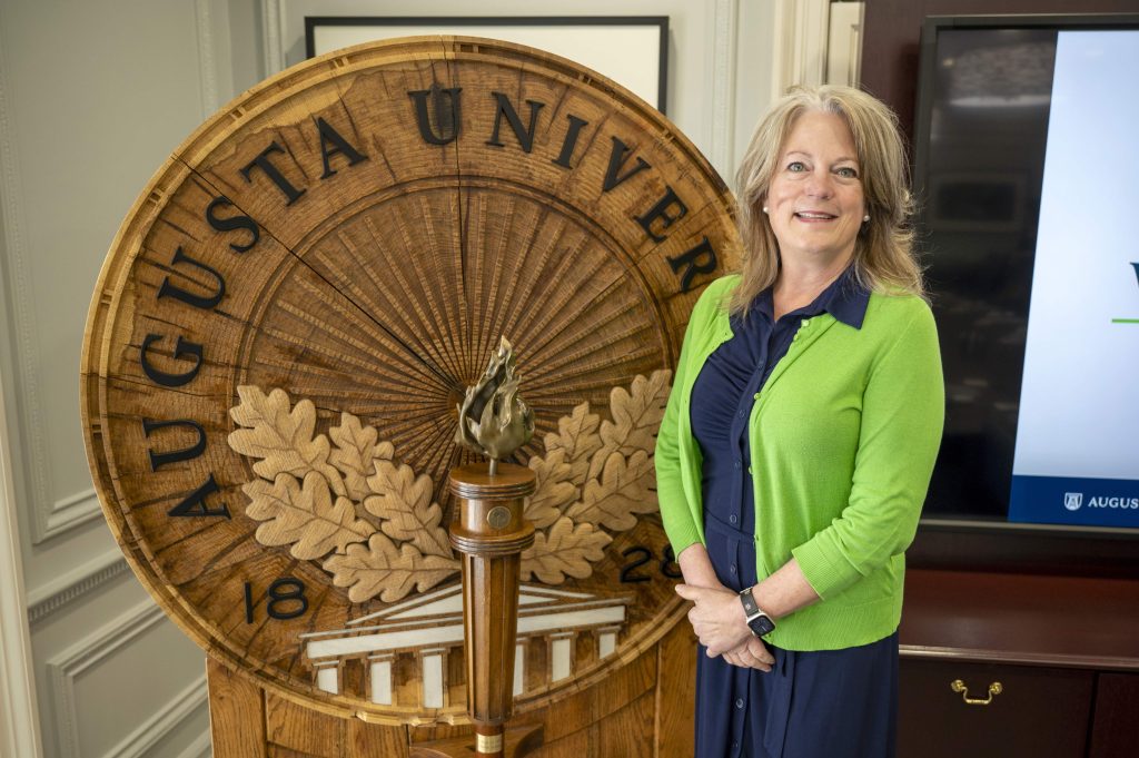 A woman poses beside the Augusta University shield.