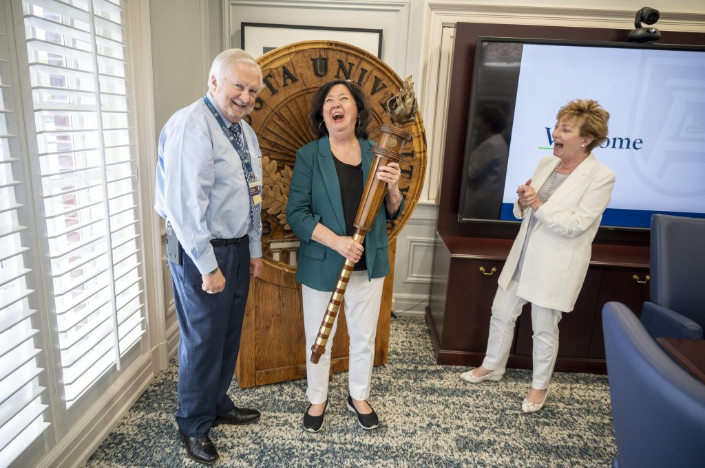 Three people pose for a photo in front of the Augusta University shield, laughing in a candid moment.