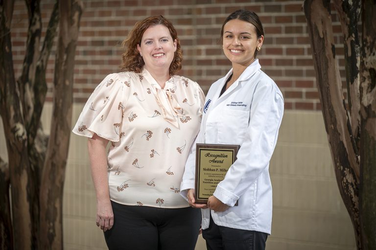 Two women smiling with one holding a plaque