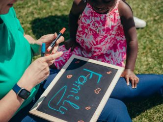 A young child sits outside in the grass with a woman holding a chalkboard that says family