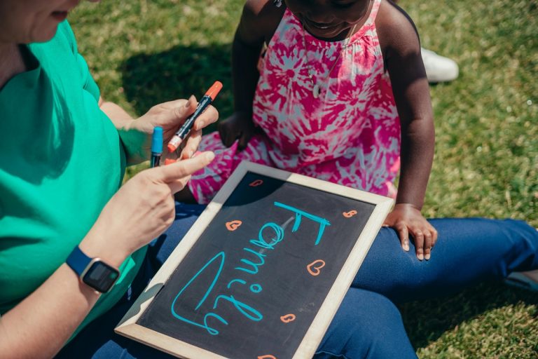 A young child sits outside in the grass with a woman holding a chalkboard that says family