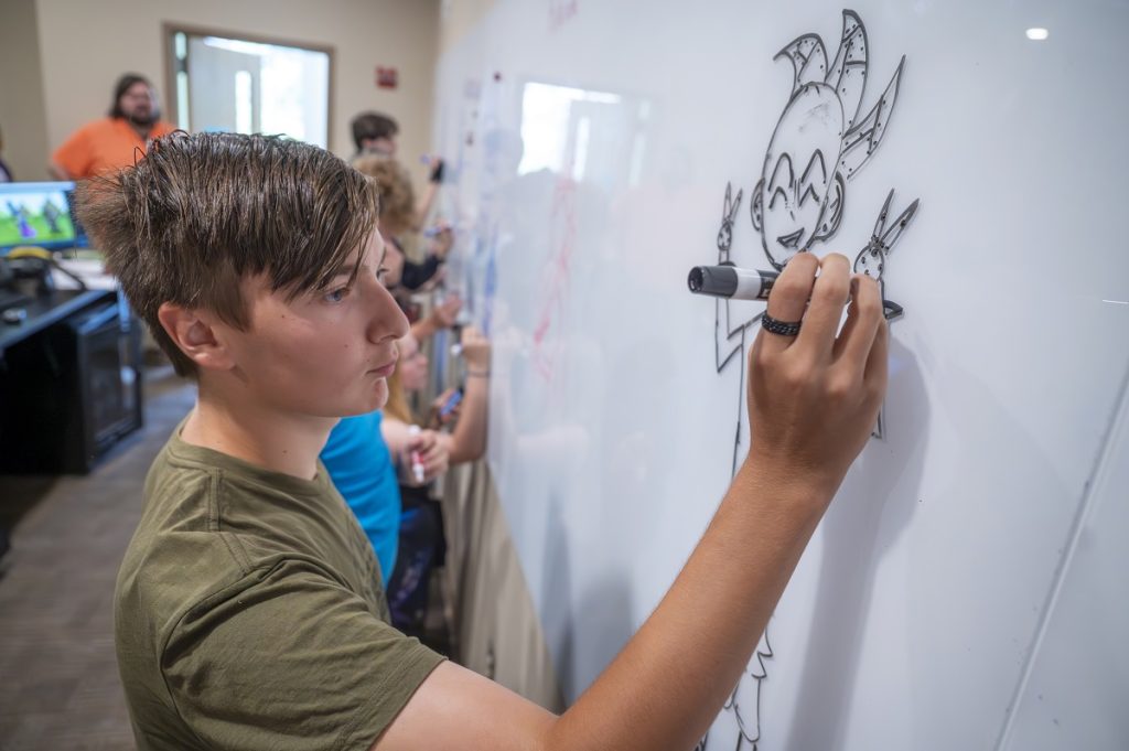 A student comes up with a character on a whiteboard during animation camp