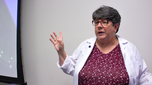 A woman wearing a medical professional's lab coat instructs a classroom full of nursing students.