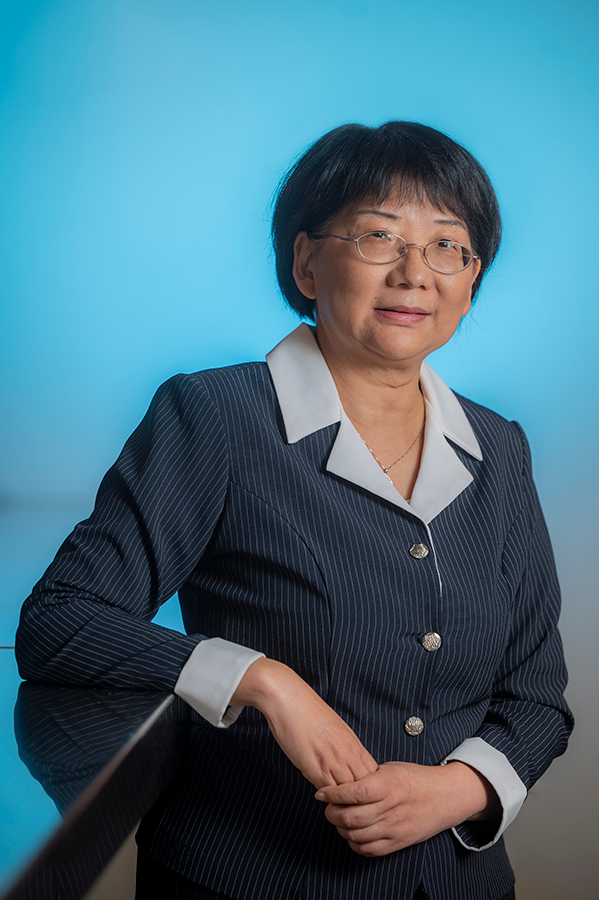 A woman in a business suit leans against a table top.