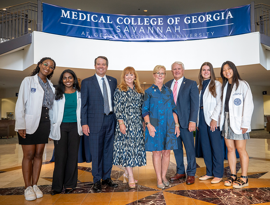 A group of people stand in a large atrium. There is a banner behind them that reads, "Medical College of Georgia Savannah at Georgia Southern University."