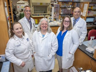 group in white coats stands in lab