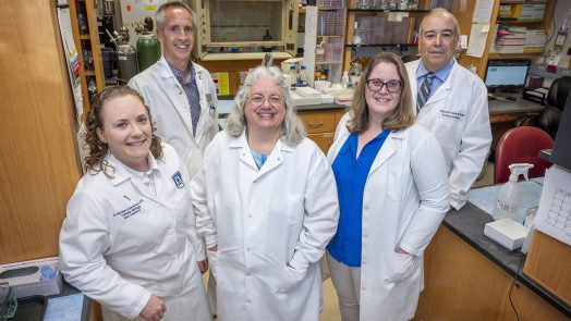 group in white coats stands in lab