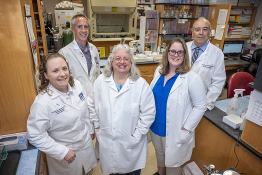 group in white coats stands in lab