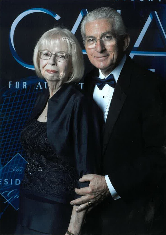 An older man wearing a tuxedo and woman wearing a gown stand next to each other. 