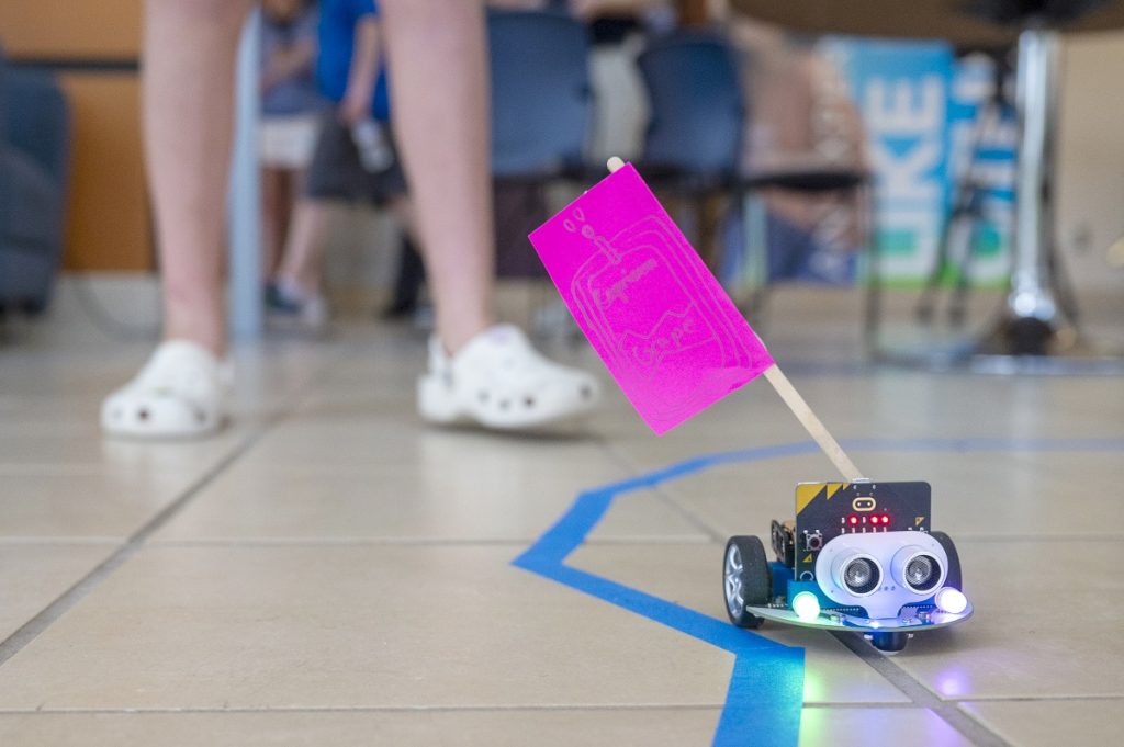 A microbot, a kind of radio-controlled car, drives over a course of masking tape on the floor.