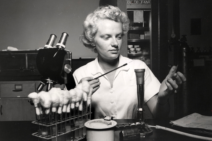 A woman sits at a laboratory bench and works with lab equipment.