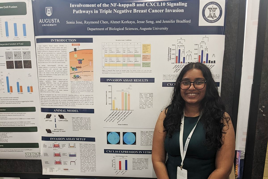 A female college student stands in front of a large poster depicting research she has conducted.