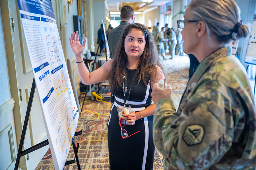 A woman speaks to a female soldier about information on a poster with research information.