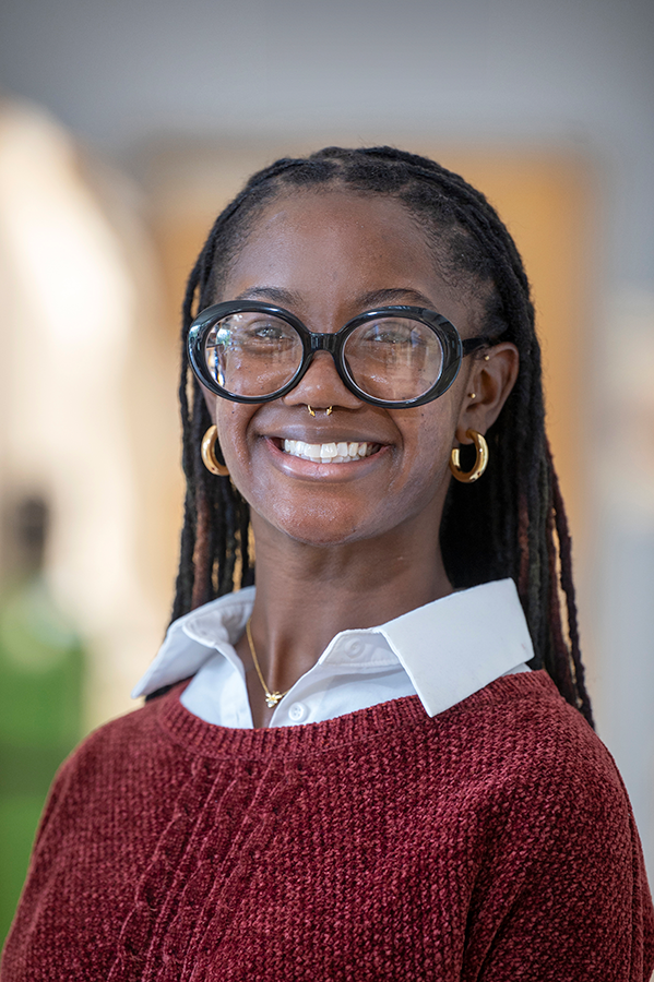 A female graduate student wearing glasses stands inside a scientific lab and poses for a photo.