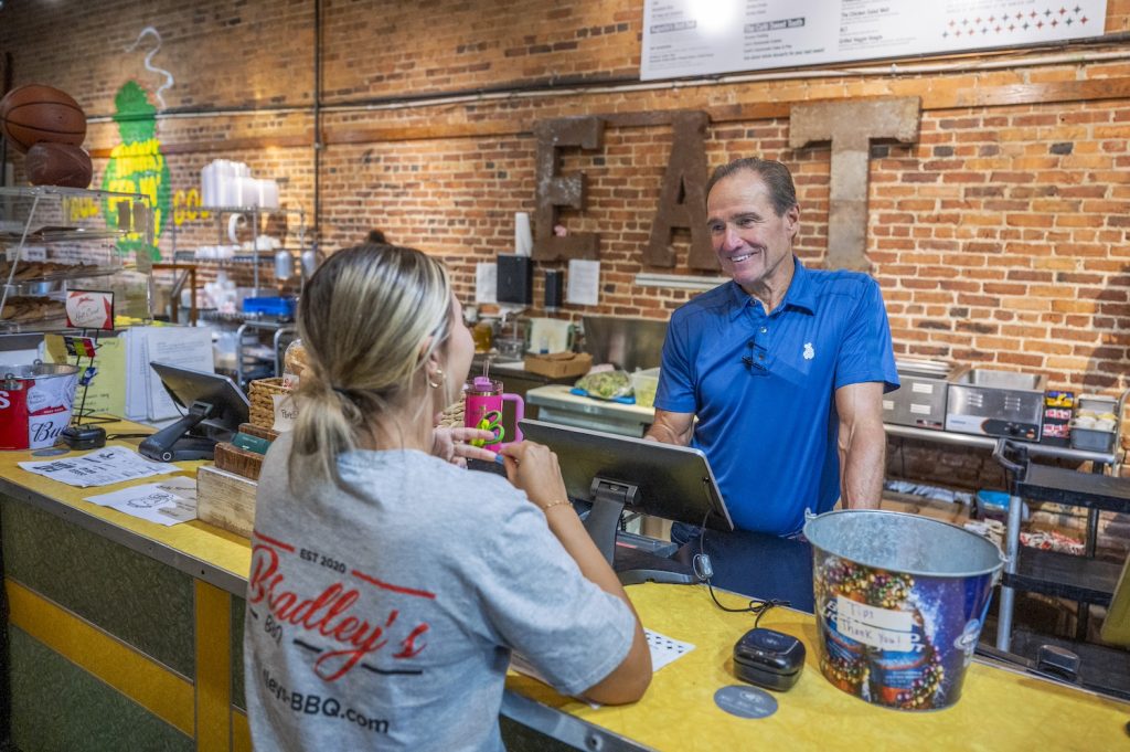 A man in a blue shirt stands behind the counter, taking a customer's order.