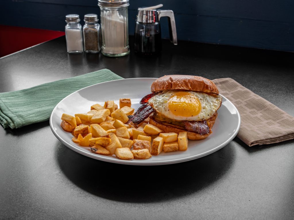 Breakfast sandwich of fried egg and bacon and homefries.