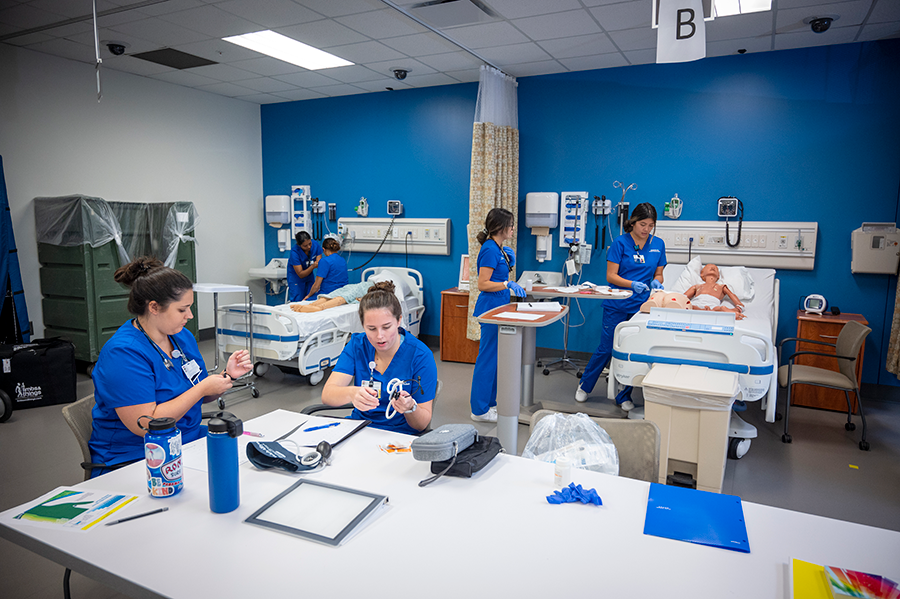 College students studying to be nurses practice what they have learned inside a practice lab that is set up to look like a hospital room.