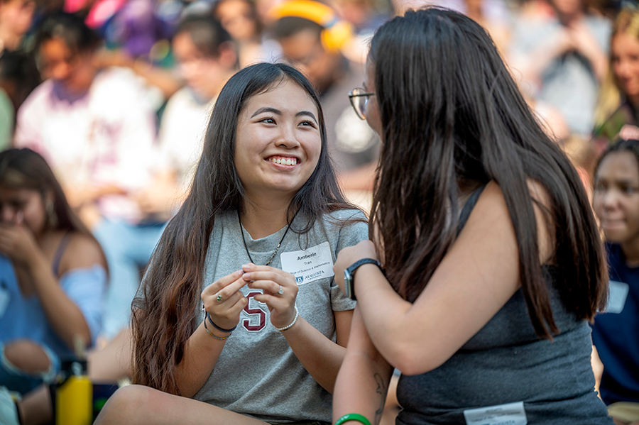 Two college freshmen women talk to each other during an outside gathering.