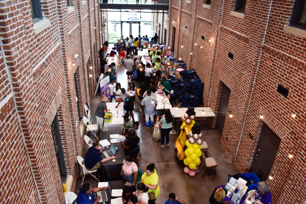 A large crowd of families visit different booths spread out in a large building celebrating back to school season.