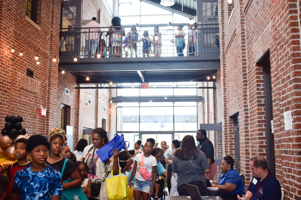 A large crowd of families visit different booths spread out in a large building celebrating back to school season.