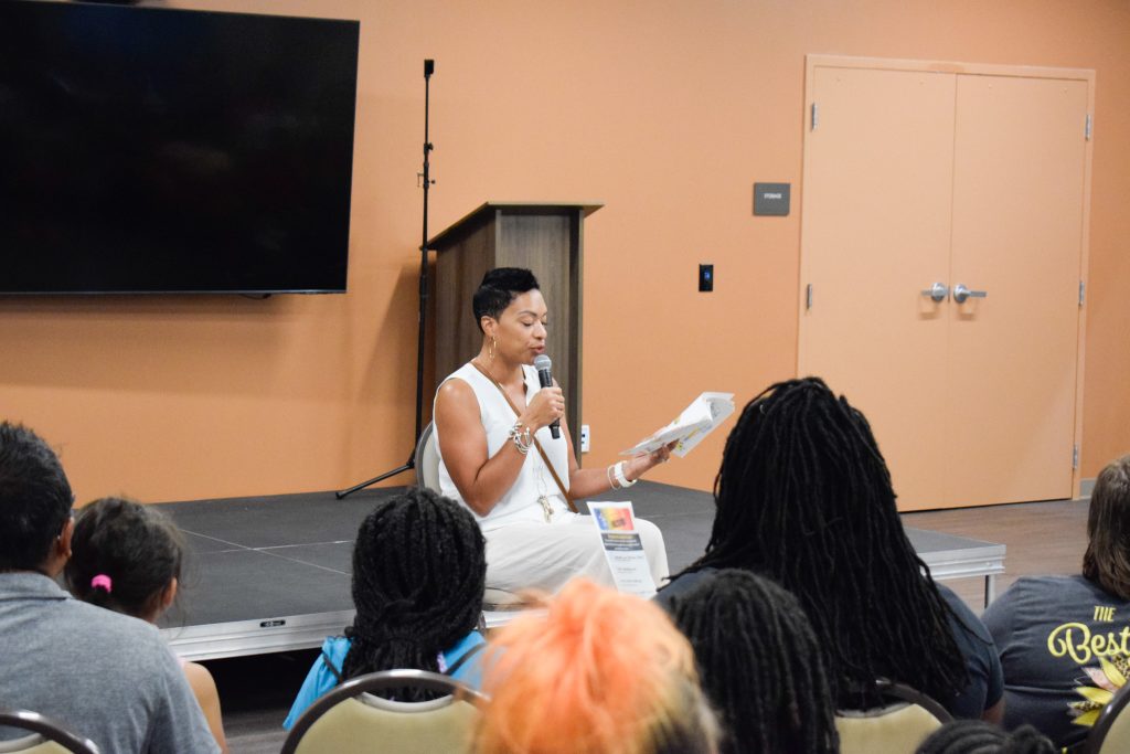 A woman sits on a stage and reads to a large group of people.