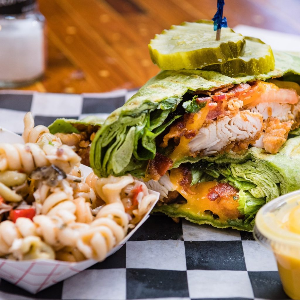 A wrap made of lettuce around cheese, ham and other toppings sits on a plate next to pasta salad.