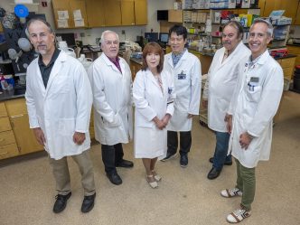 Group of medical researchers, all wearing lab coats, standing in a lab.