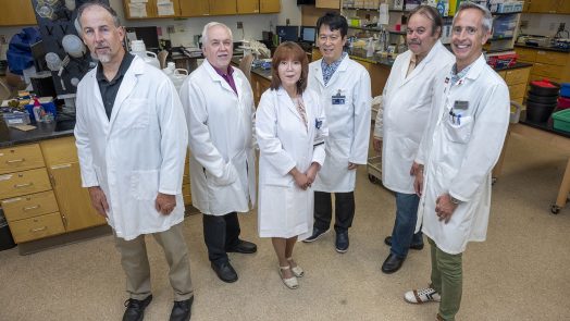 Group of medical researchers, all wearing lab coats, standing in a lab.