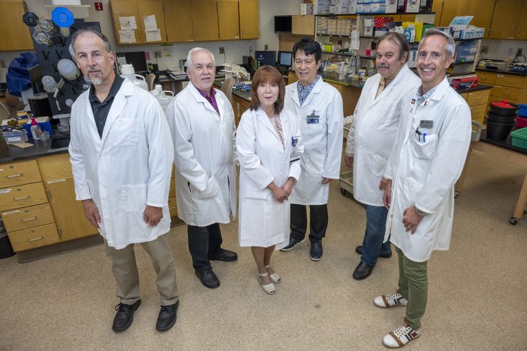 Group of medical researchers, all wearing lab coats, standing in a lab.