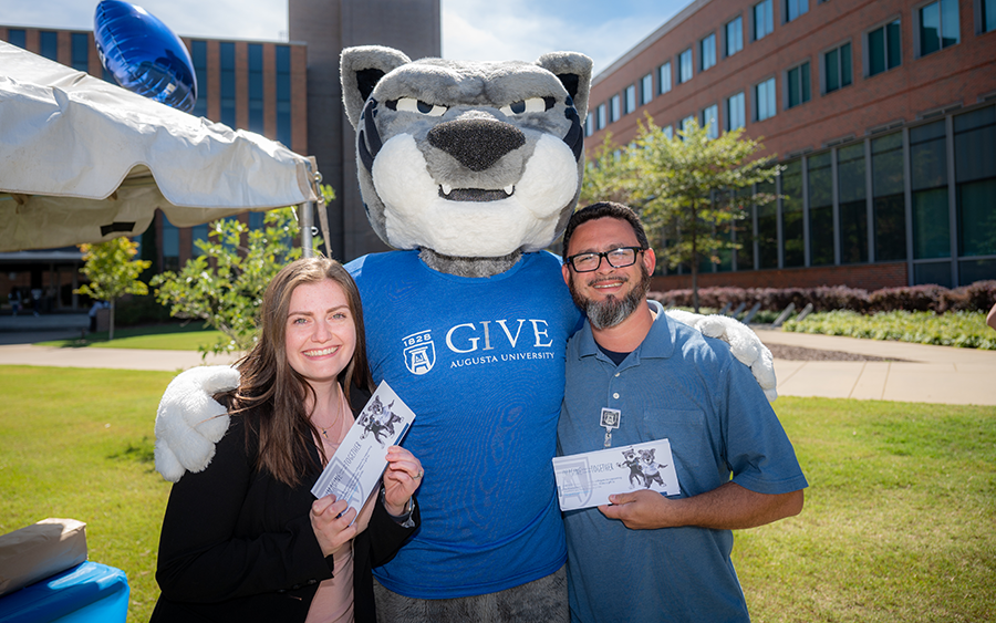 A college mascot depicting a jaguar stands outside with two people.