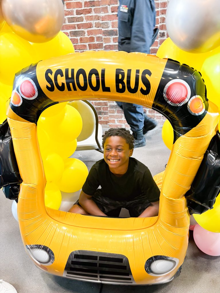 An elementary school boy kneels down inside an inflatable school bus.