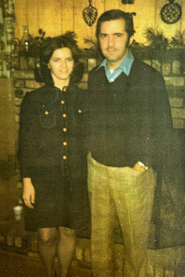 An old yellowed-out photo of a woman and a man standing in front of a fireplace.