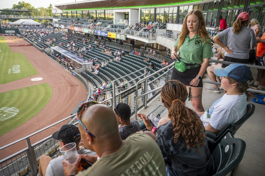 A young woman talks with patrons at a baseball game.