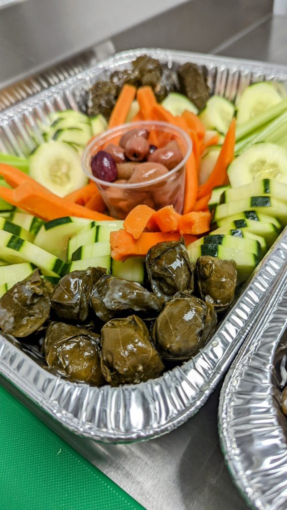 An aluminum pan of assorted vegetables, including brussel sprouts, cucumbers, carrots and olives.