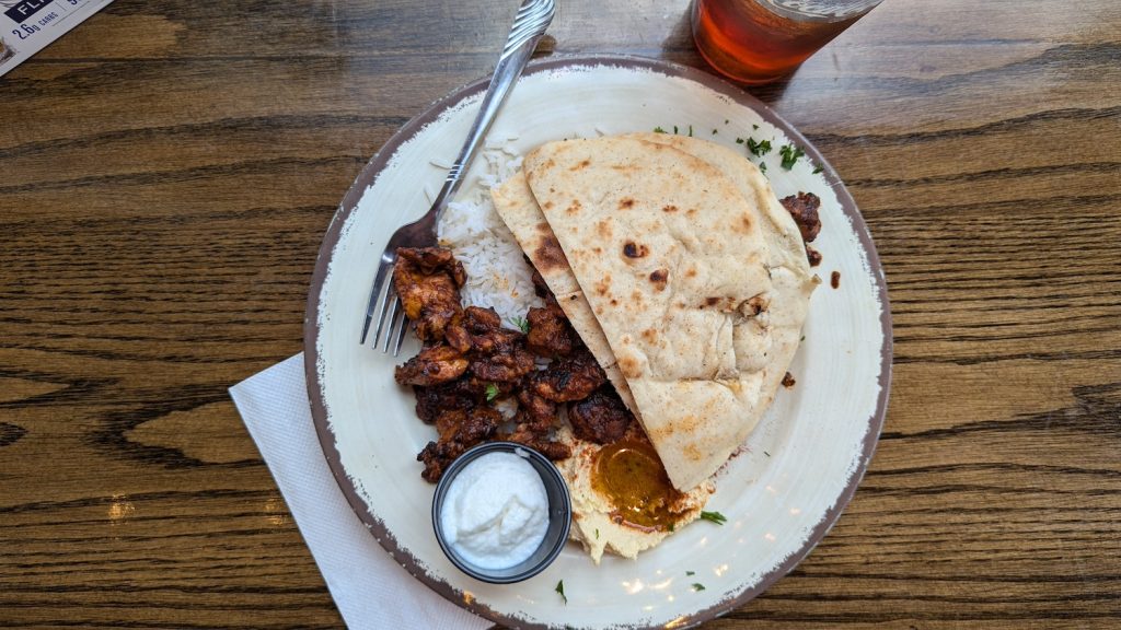 Naan bread, rice, grilled chicken, hummus and a dipping sauce sit on a plate.