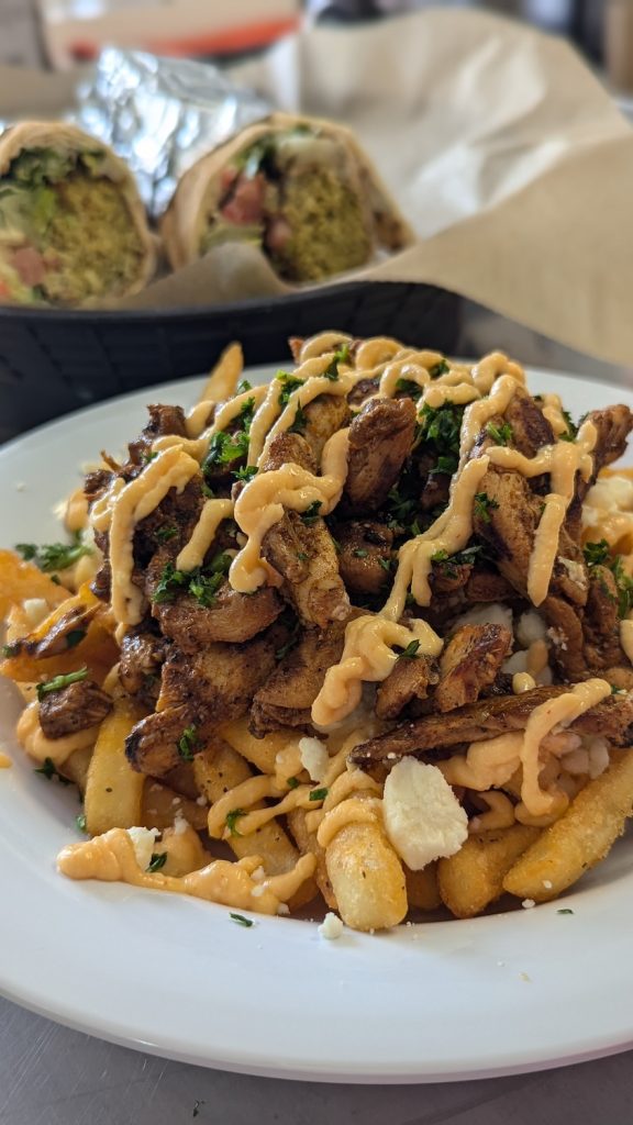 A plate of loaded fries topped with feta cheese, chopped chives, and a sauce.