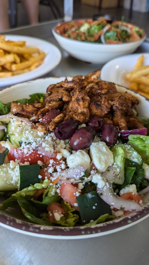 A Greek salad topped with feta cheese, olives, cucumbers, tomatoes, onions and grilled chicken.