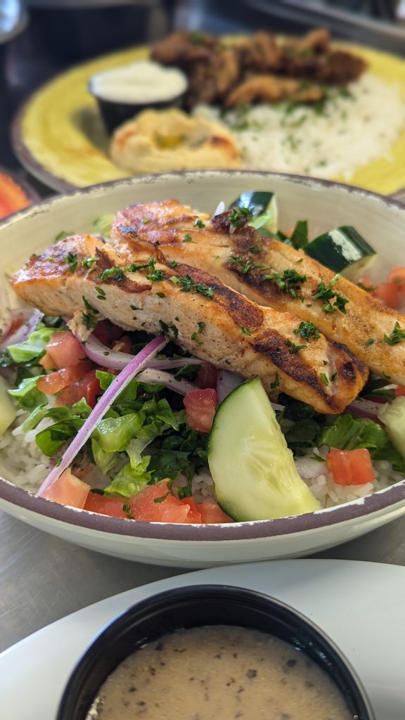 A dish containing rice, shredded lettuce, cucumbers, pico de gallo, grilled chicken breast and other vegetables.