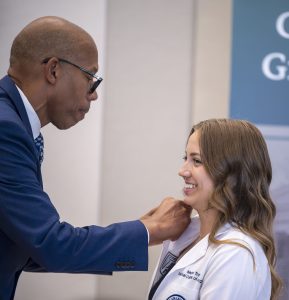 Man in glasses places pin on medical lab coat of a college girl.