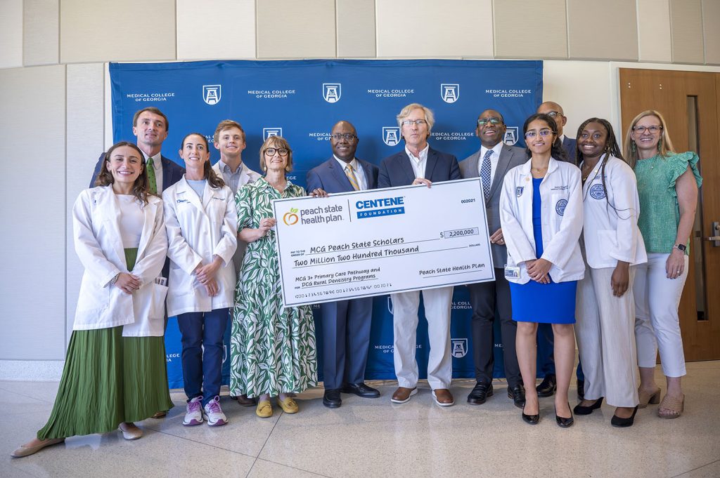 people stand in front of backdrop with logos for Augusta University and the Medical College of Georgia printed on it. The four people in the middle are holding an oversized check.