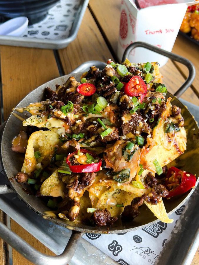 A bowl holding nachos loaded with steak, jalapenos, chopped chives, cheese and other toppings.