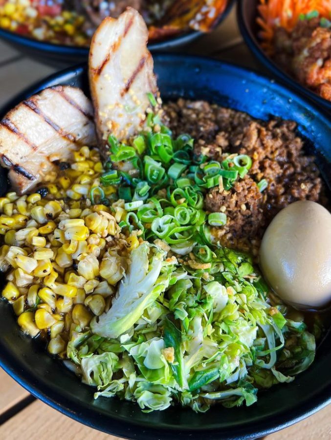 A dish that contains a boiled egg, corn, shredded lettuce, ground beef, chopped chives and grilled chicken breasts.