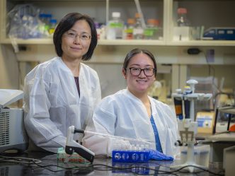 Two women in lab coats sit behind lab bench