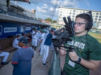 College student holds a camera outside a baseball dugout