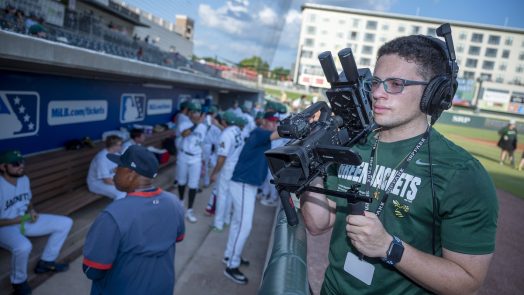 College student holds a camera outside a baseball dugout