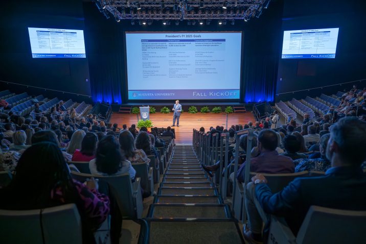 A man delivers a presentation on stage in front of an audience of hundreds.